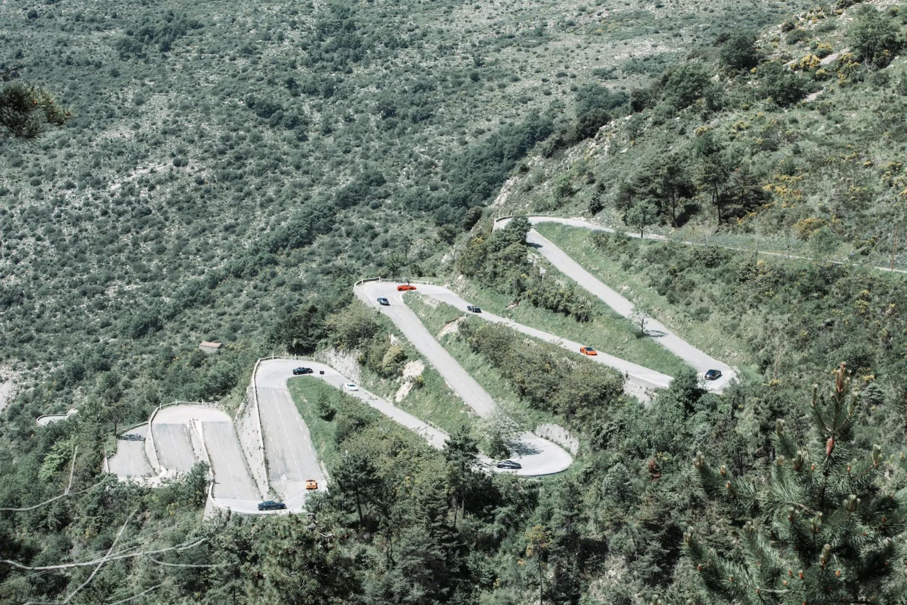 supercars climb up a hill with a series of hairpin turns on a clear day