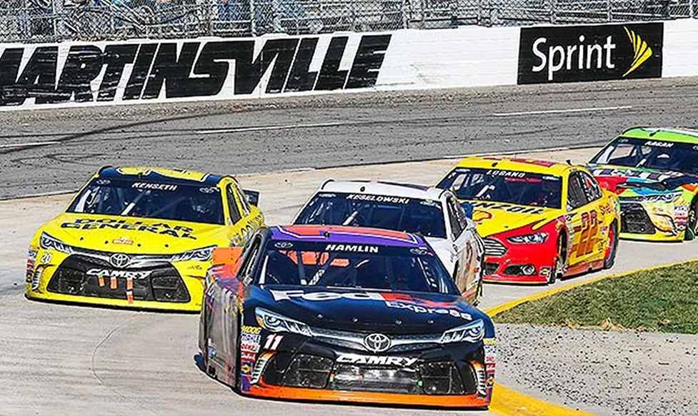 A tightly bunched group of NASCAR race cars approach a corner at Martinsville Speedway, Greensboro