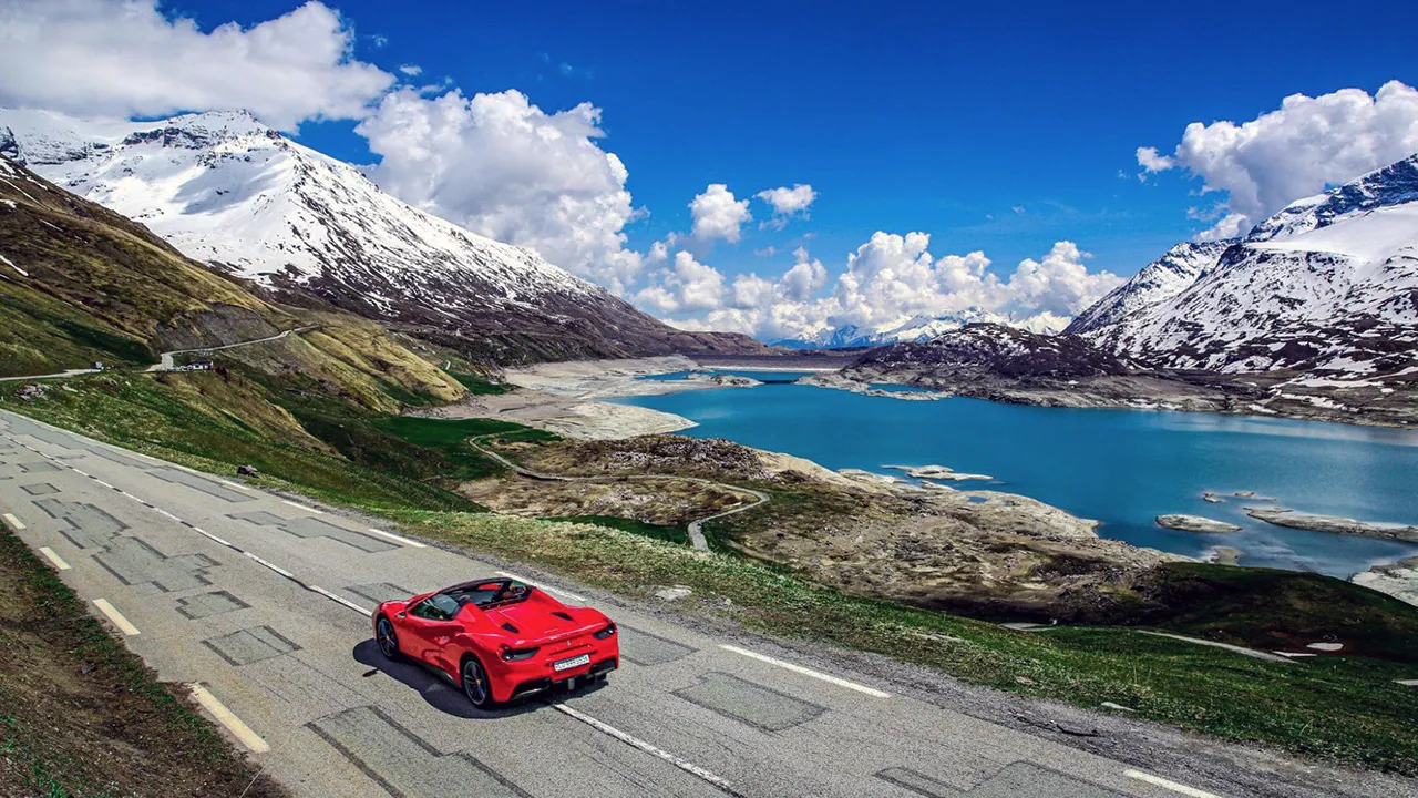 A red supercar driving alongside a lake and snow-capped peaks