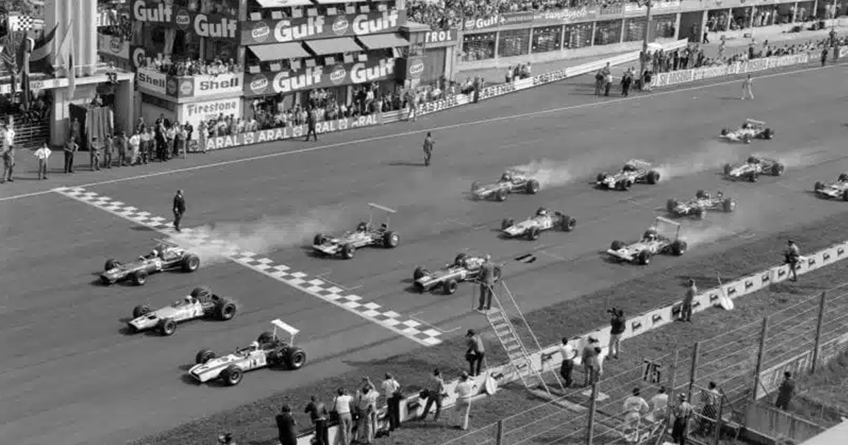 Black and white image of vintage Formula 1 cars as they race off the line leaving clouds of smoke behind.