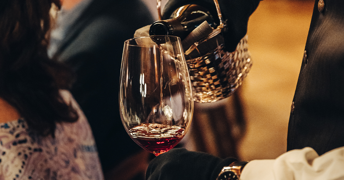 An elegant tall wine glass being filled with red wine by a waiter.