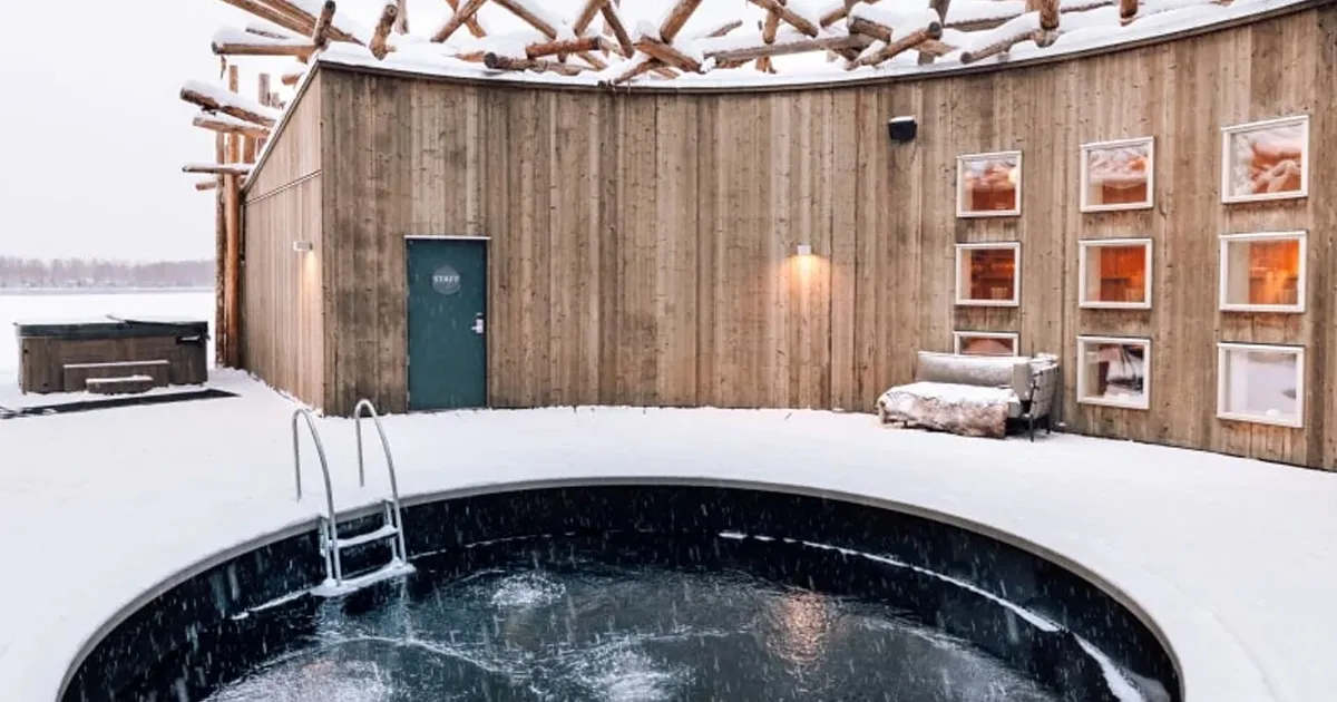 An outdoor arctic bath with bubble jets in front of a snow-covered timber bathhouse.