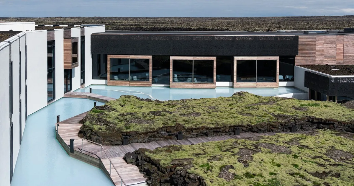 Moss covered rock structures are surrounded by wooden walkways and bright blue waters at the geothermal blue lagoon spa in Iceland.