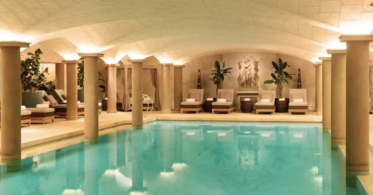 A lavish indoor swimming pool with marble finish surrounded by large columns, designer sun loungers and sculptures at Grantley Hall, United Kingdom
