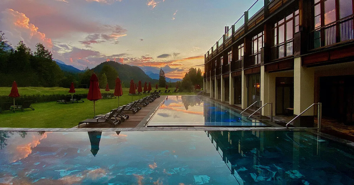 Sunset over an artistic outdoor pool area and lush green grounds in the Bavarian Alps at Schloss Elmau resort.