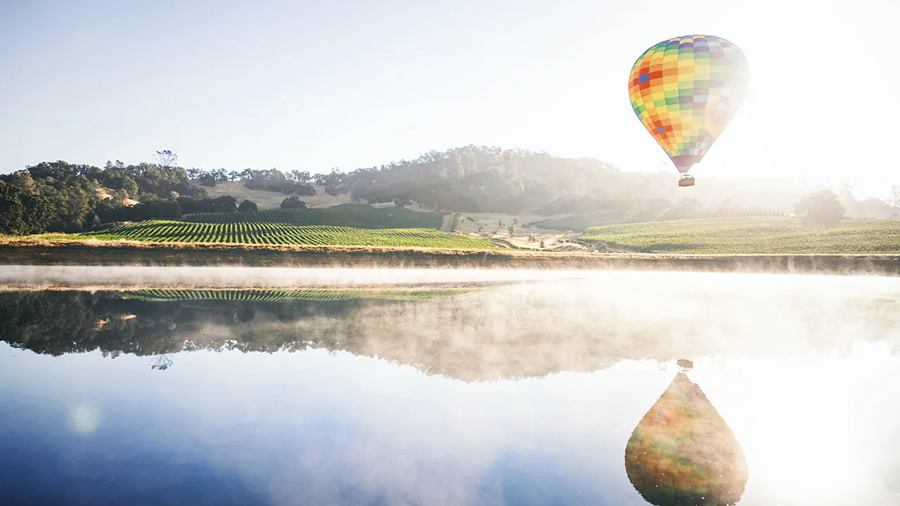 A colourful hot air balloon cruises over a body of water in Napa Valley, California