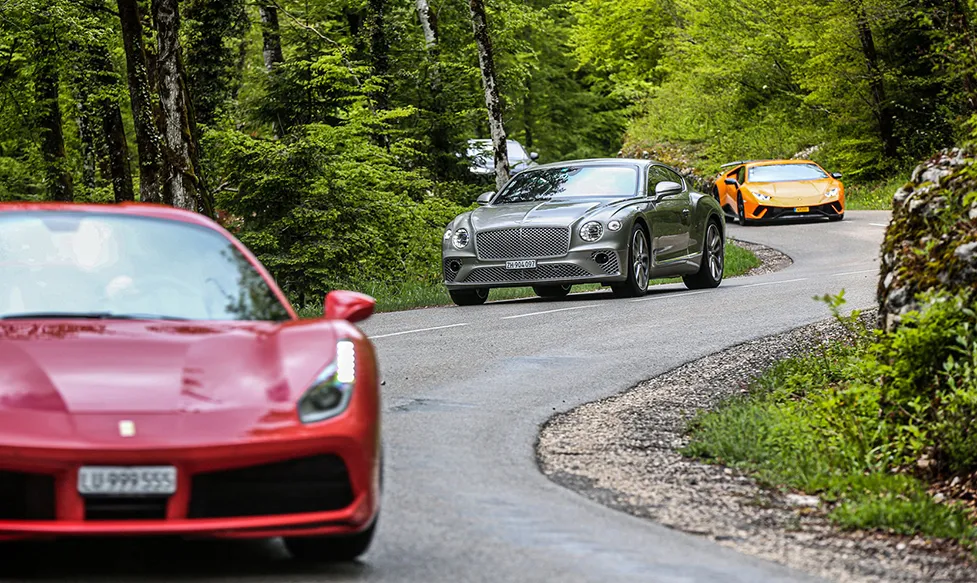 A Ferrari leads a Bentley followed by a Lamborghini as they drive through the Black Forest in Germany
