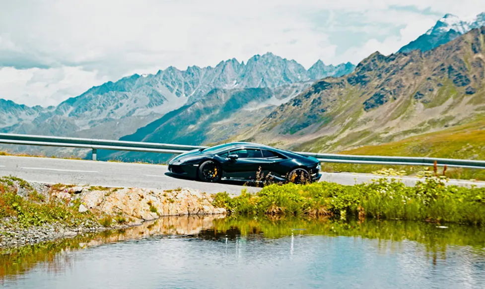 A black Lamborghini Aventador climbs an alpine pass