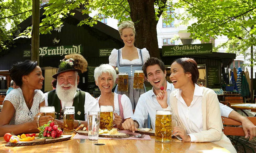A group of people drinking beer as they sit around a table outdoors at Oktoberfest, Munich, Germany