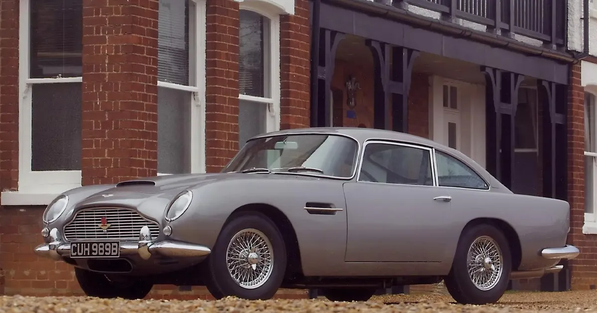 A dark silver Aston Martin DB5 sitting outside a red brick building.