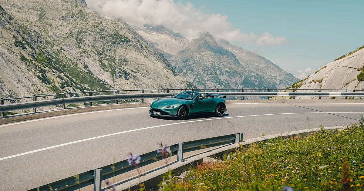 A teal coloured Aston Martin Vantage F1 Roadster rounds a corner during an Ultimate Driving Tours luxury tour.