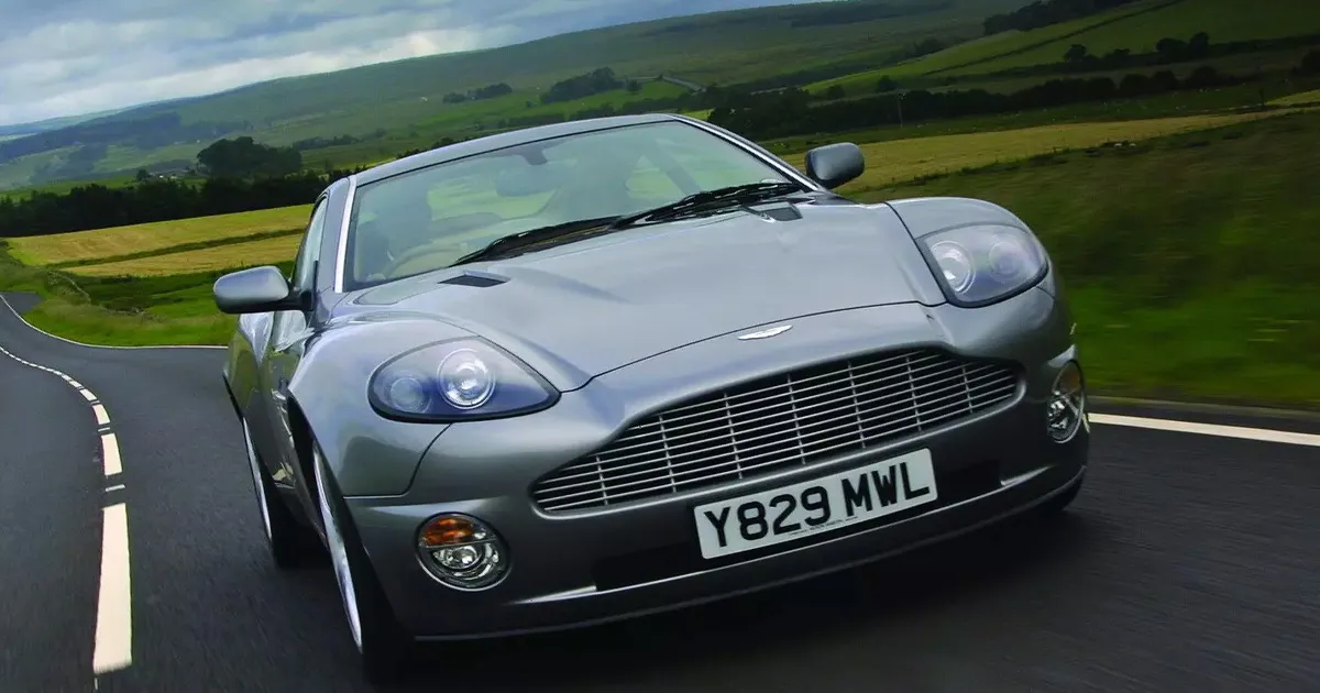 A dark silver Aston Martin Vanquish cruising on a country road.