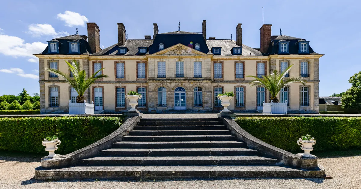 A large sandstone château with flax bushes and sweeping stone steps.