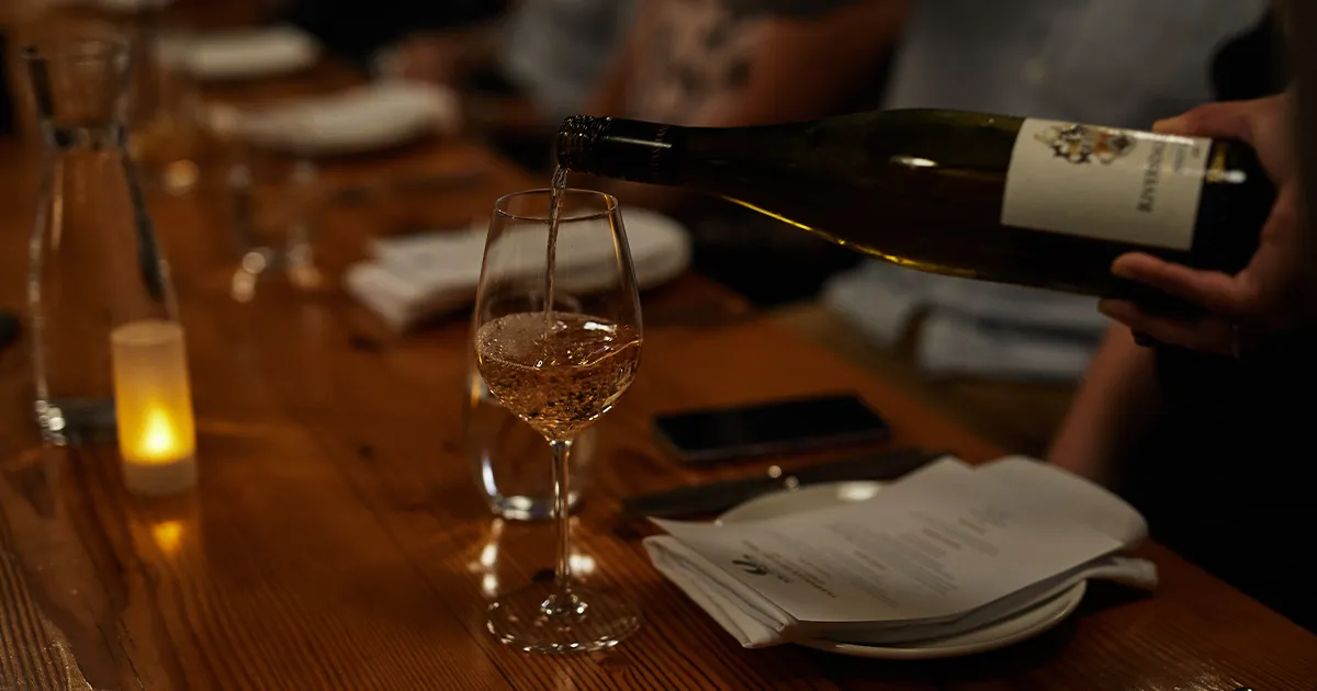 A white wine is carefully poured into a glass on a candlelit dinner table.