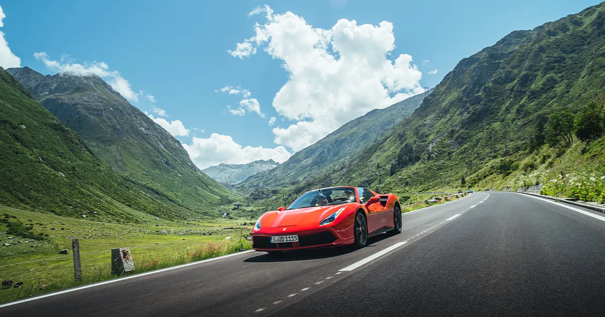 A red Ferrari drives through a green Swiss valley on a supercar tour.