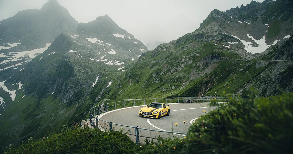 A cloudy day as a yellow Mercedes-Benz AMG GT rounds a corner in the Swiss Alps.
