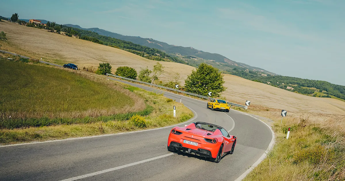 A yellow Mercedes AMG GT leads a red Ferrari 488 Spyder round a sweeping corner in Tuscany