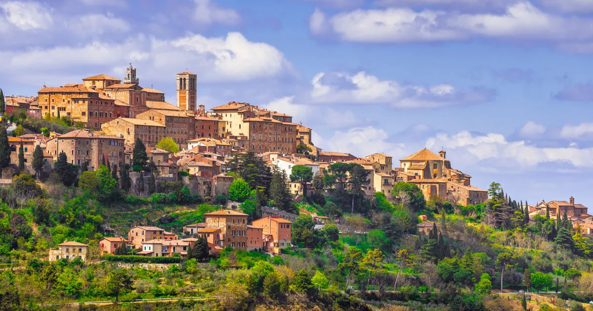 Montepulciano seen from below with red brick buildings, clay roofs and cloudy sky.