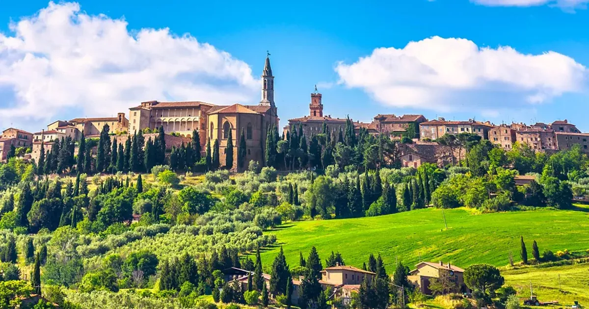 Pienza, Tuscany with cypress trees, ornate stone buildings and verdant hills.