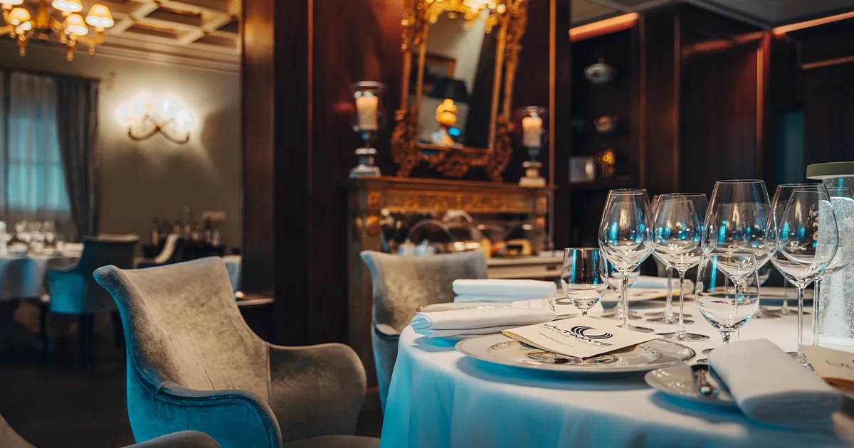 A classically French dining room with an ornate mirror, wooden trim and luxurious chairs.