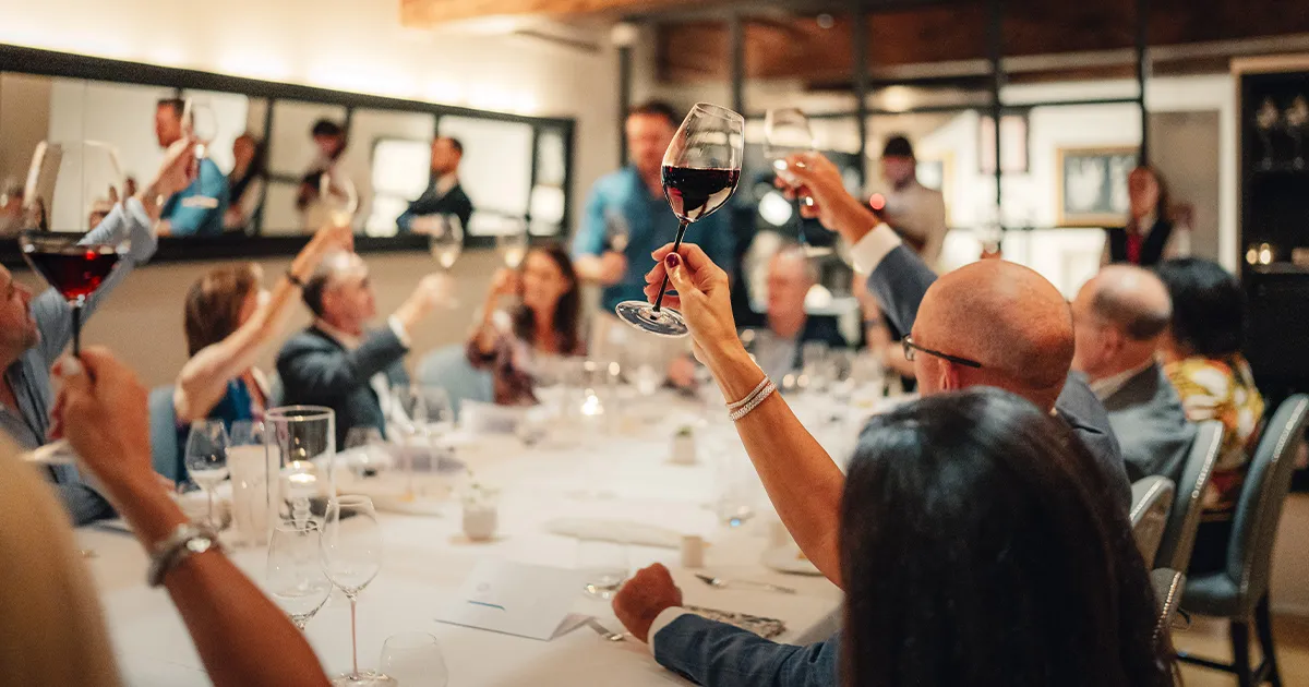 Dinner guests raise their glasses in a toast around a large table