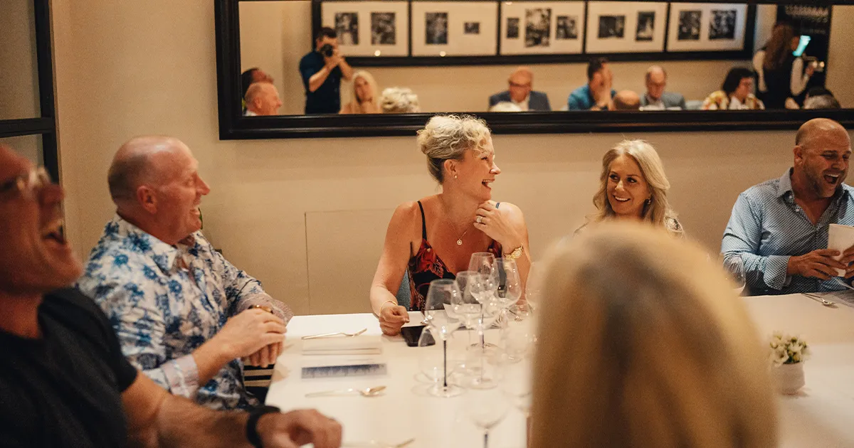 Relaxed dinner guests share a laugh around a large fine dining restaurant table