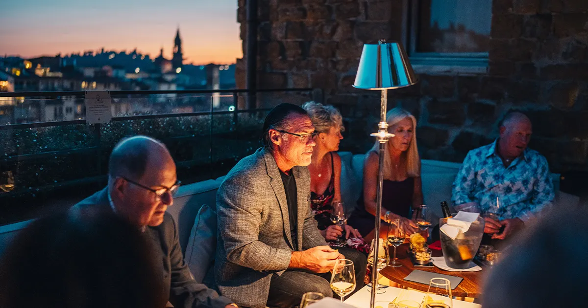A group of smartly dressed Ultimate Driving Tours guests conversing on a Florence rooftop during the evening