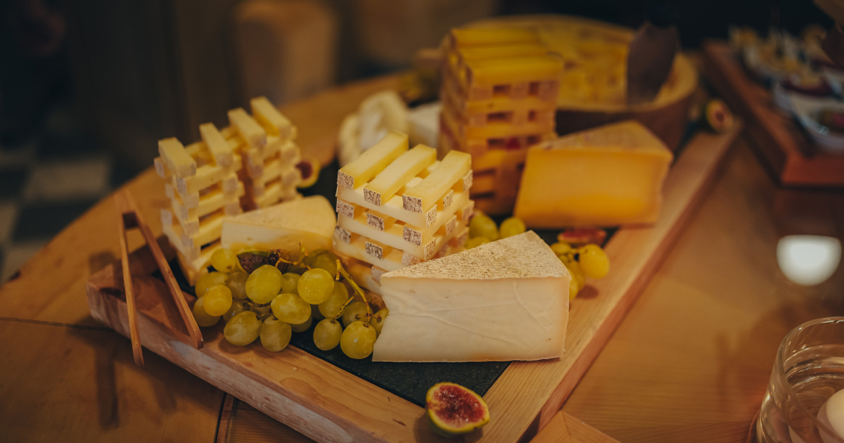 European hard cheeses arranged artistically with green grapes on wooden board