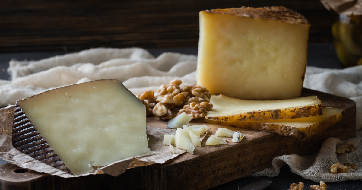 A wedge of manchego with walnuts and other hard cheese on a wooden board