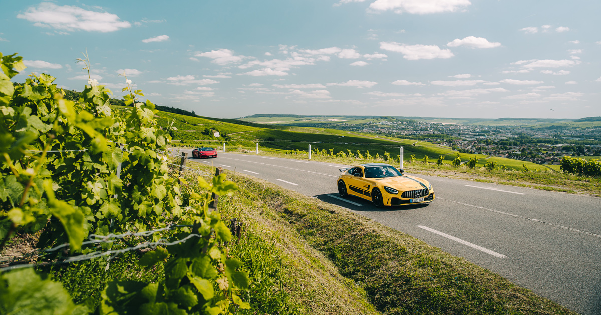 A yellow Mercedes AMG GTR rounding a corner near a vineyard in the French countryside