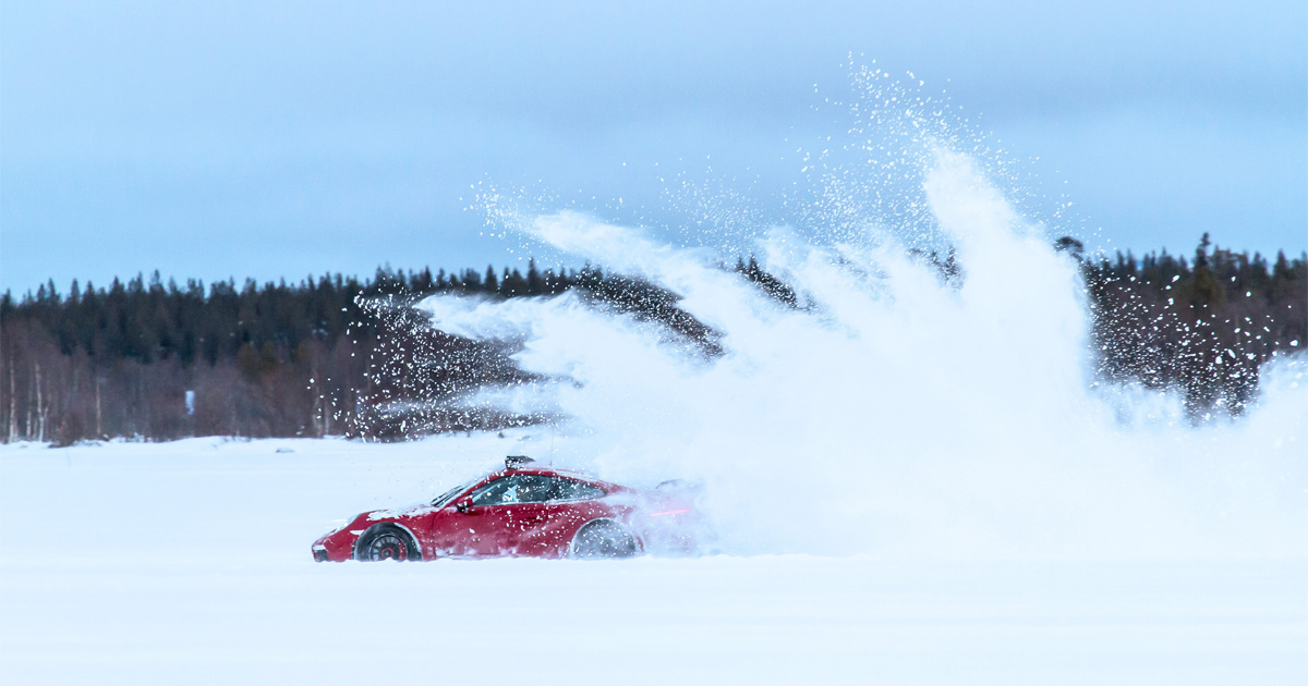 A red Porsche creates a dramatic ‘rooster tail’ snow drift in front of a forest