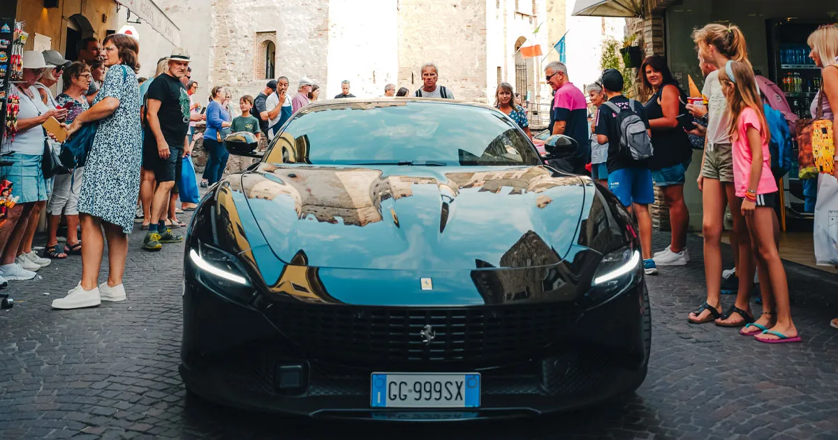 A black Ferrari Roma weaves its way through an adoring crowd of onlookers in Italy