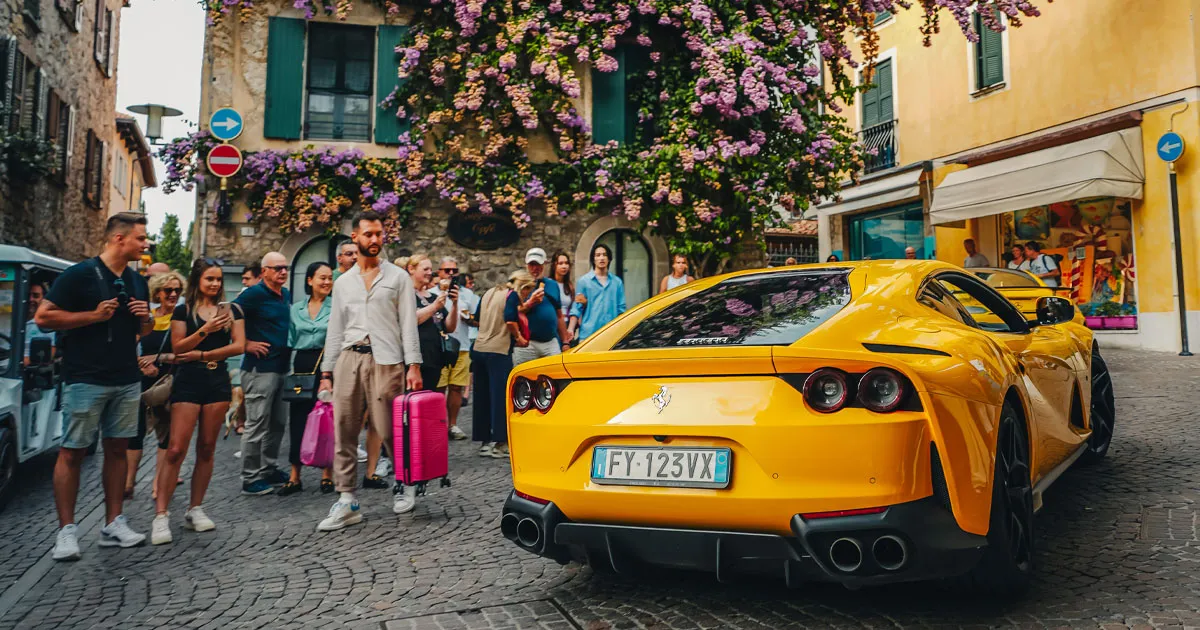 A yellow Ferrari 812 navigates tight backstreets in Italy as people stop and stare