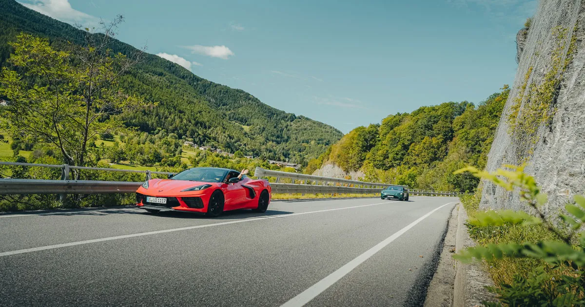 An orange Chevrolet Corvette leads a green Aston Martin on an Ultimate Driving Tours experience.