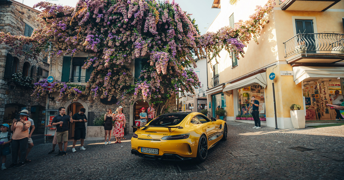 A yellow Mercedes AMG GTR pulls a crowd as it passes through a country town