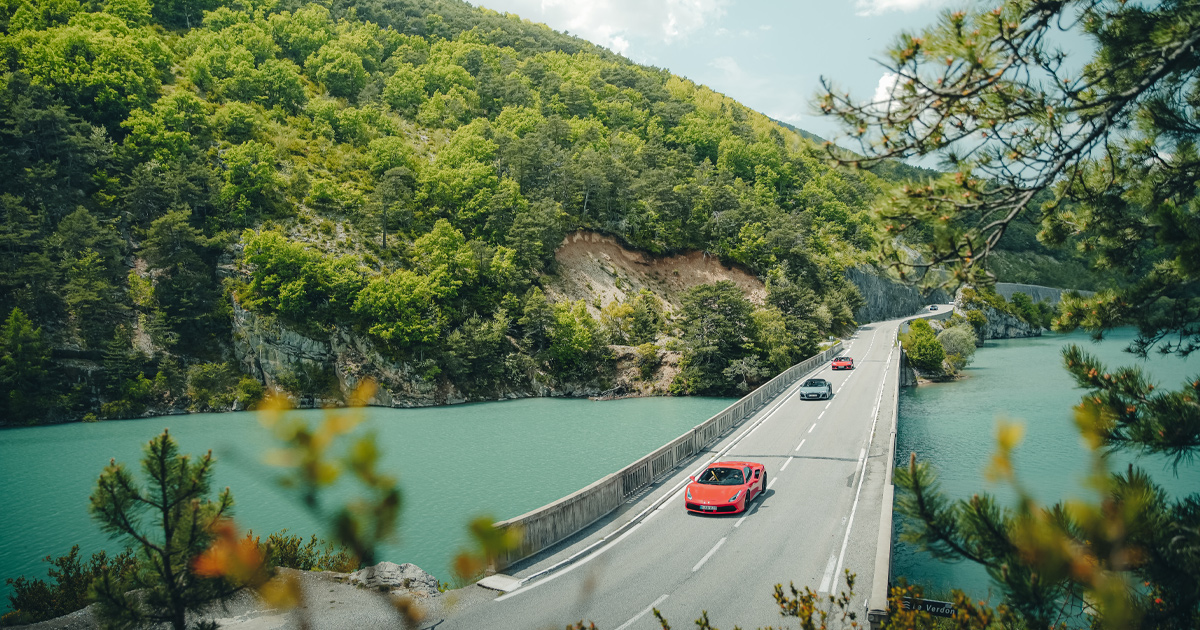 A red Ferrari 488 leads a small convoy of supercars across a bridge in Europe