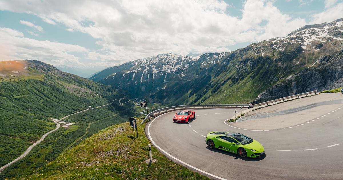A green Lamborghini Huracan leading a red Ferrari 488 round a hairpin bend in the Alps.