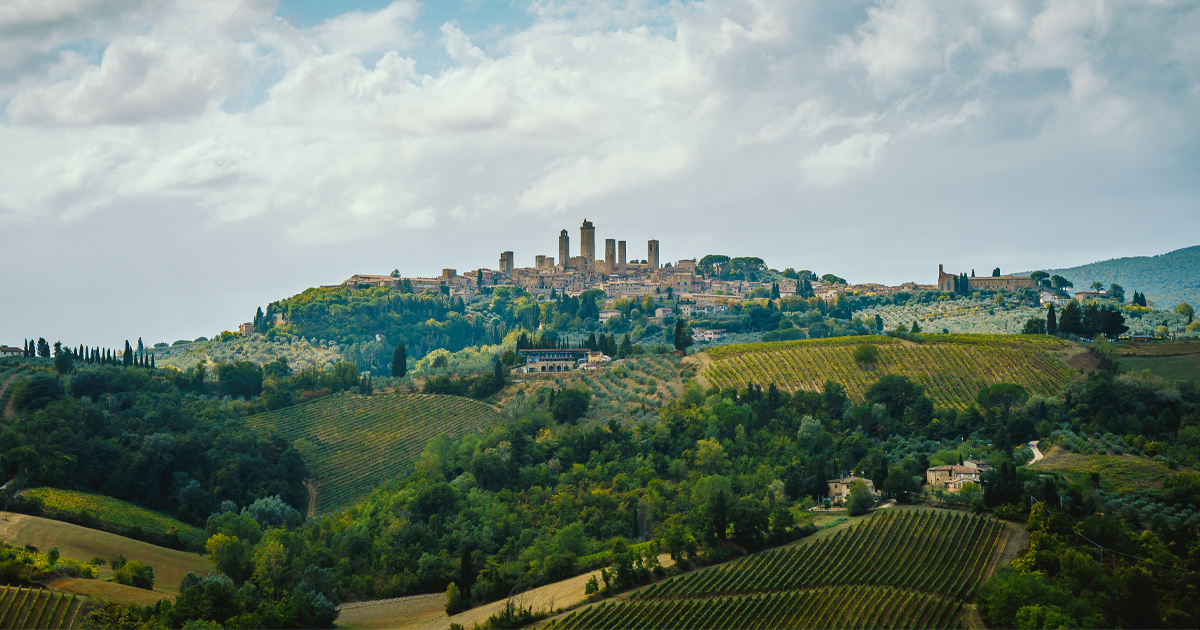 A Tuscan hilltop town seen from a distance with rolling hills in front.