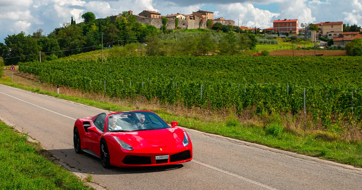 Two men drive a red Ferrari 488 Spider down a country road on an Ultimate Driving Tours experience.