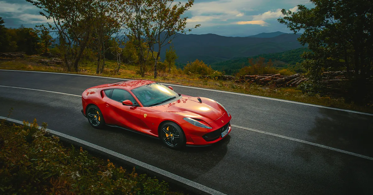A red Ferrari 812 Superfast rounds a corner on a country road.