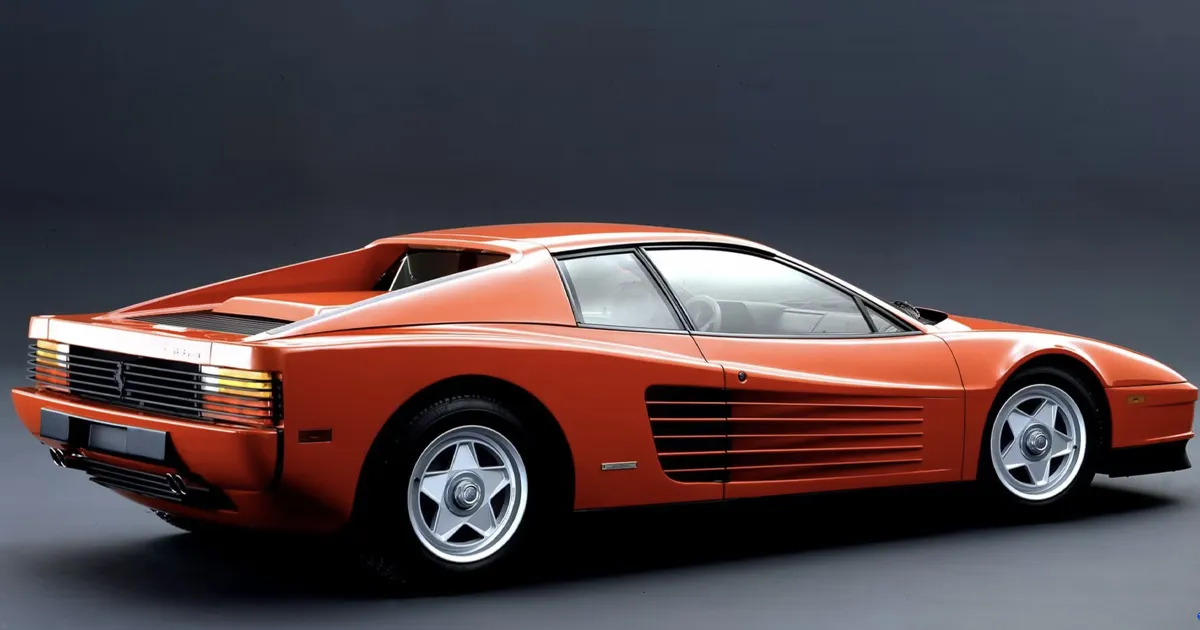 A red Ferrari Testarossa seen from a side-rear angle in a studio backdrop.