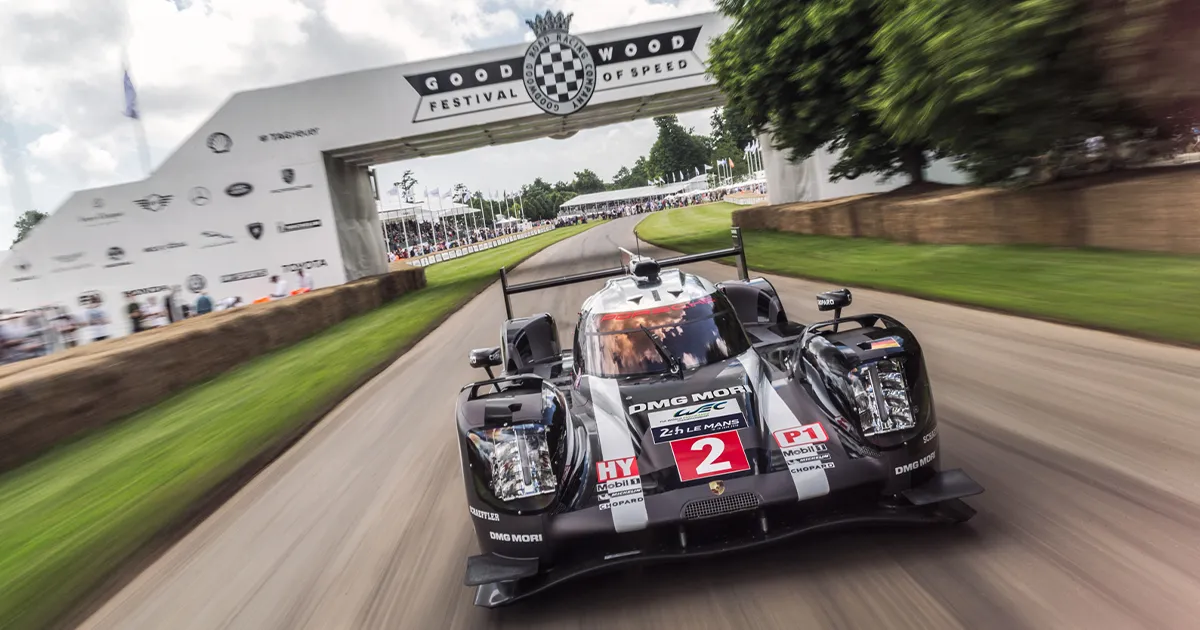 A closed-top grey modern racing car with the number 2 in red and white, speeding towards the camera on track at Goodwood, UK.