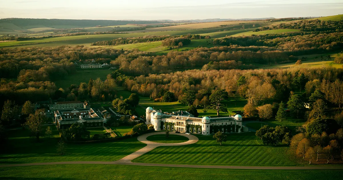 An elevated wide shot of Goodwood Estate, England, surrounded by manicured grounds and sweeping forests bathed in golden light.