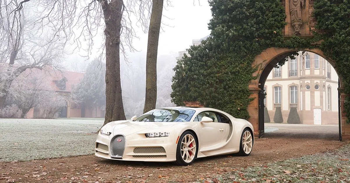 A cream coloured Hermès edition Bugatti Chiron on a driveway with a lavish archway outside a huge mansion.