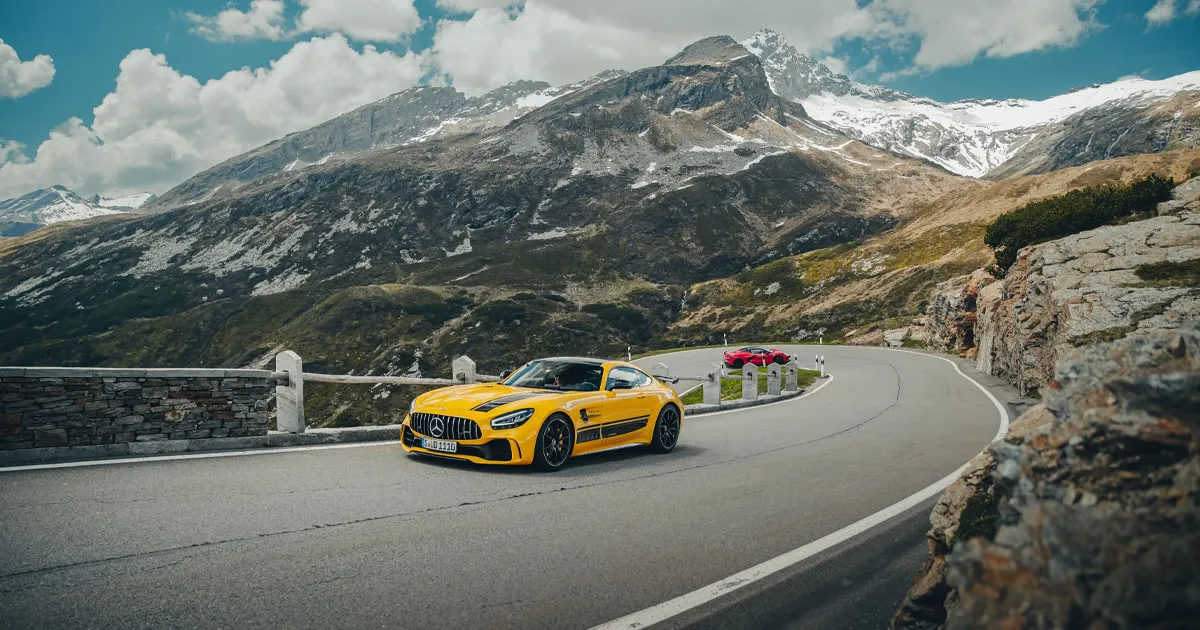A yellow Mercedes AMG GT leads a red Chevrolet Corvette around an alpine hairpin 