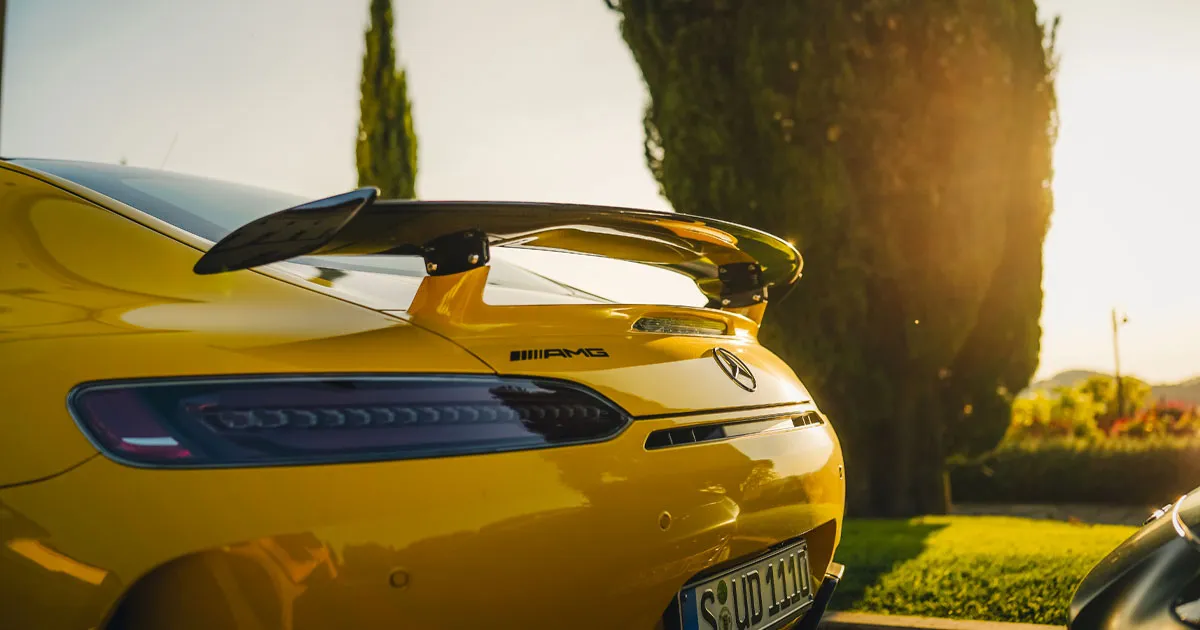 The rear spoiler of a yellow Mercedes AMG GTR gleaming in morning sunlight