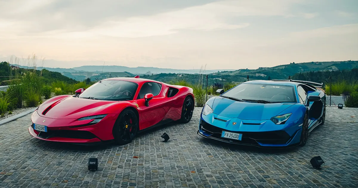 A red Ferrari SF90 and a blue Lamborghini Aventador on a cobbled driveway in Tuscany.