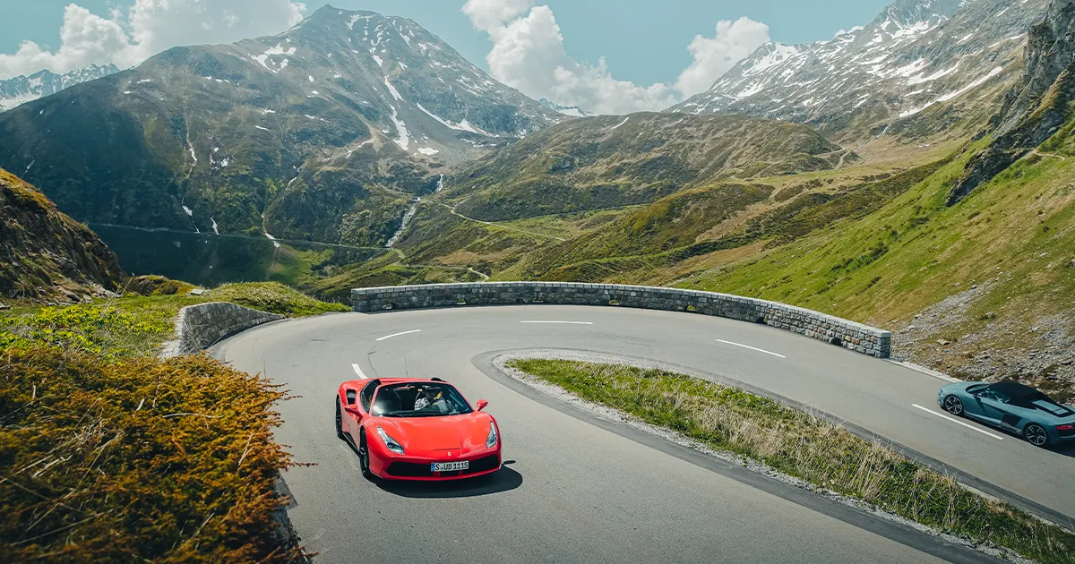A red Ferrari rounds a hairpin corner high up in the mountains.