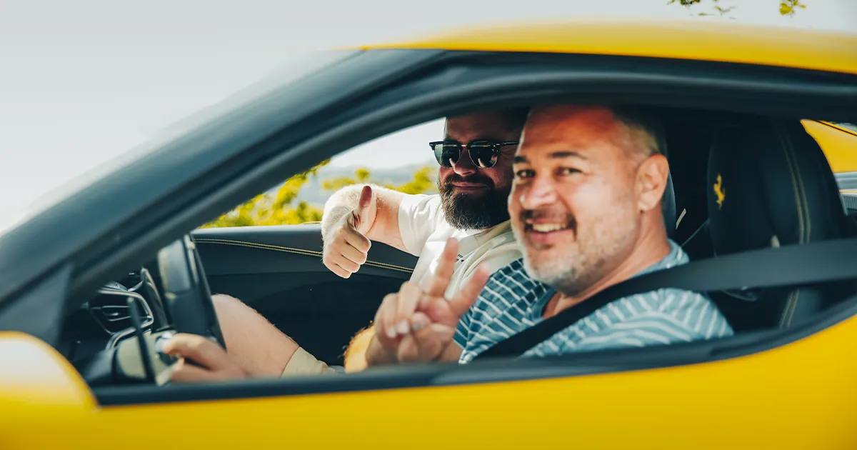 Two men happily pose for the camera while sitting in a yellow Ferrari.
