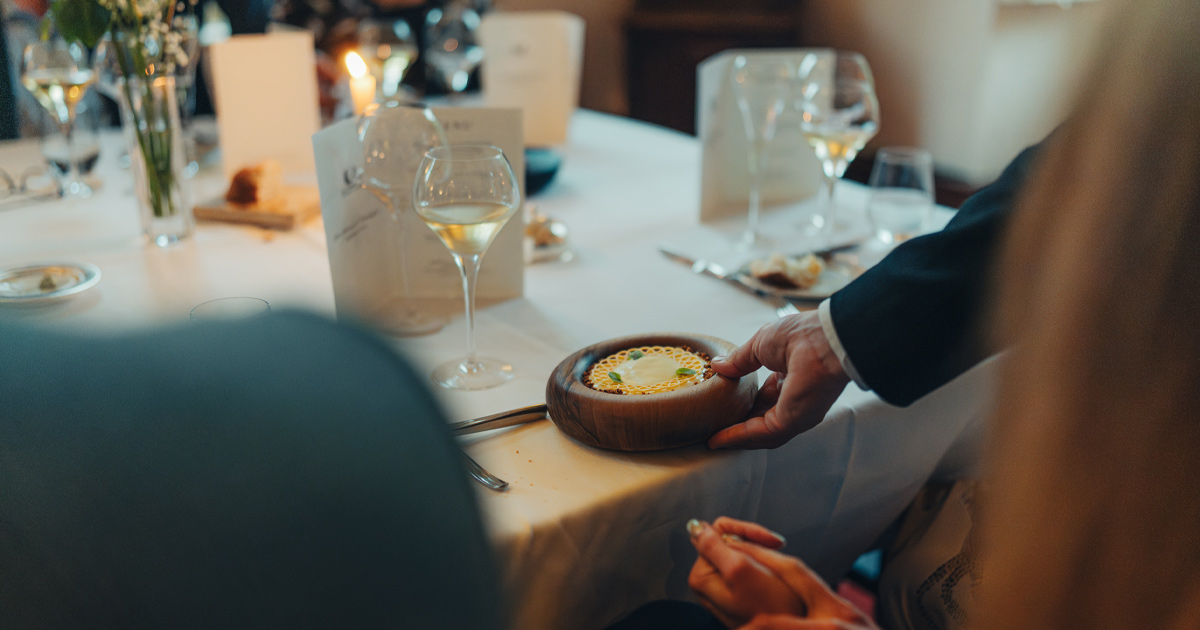 A waiter serves a wooden bowl with an artistic dish at a fine dining restaurant